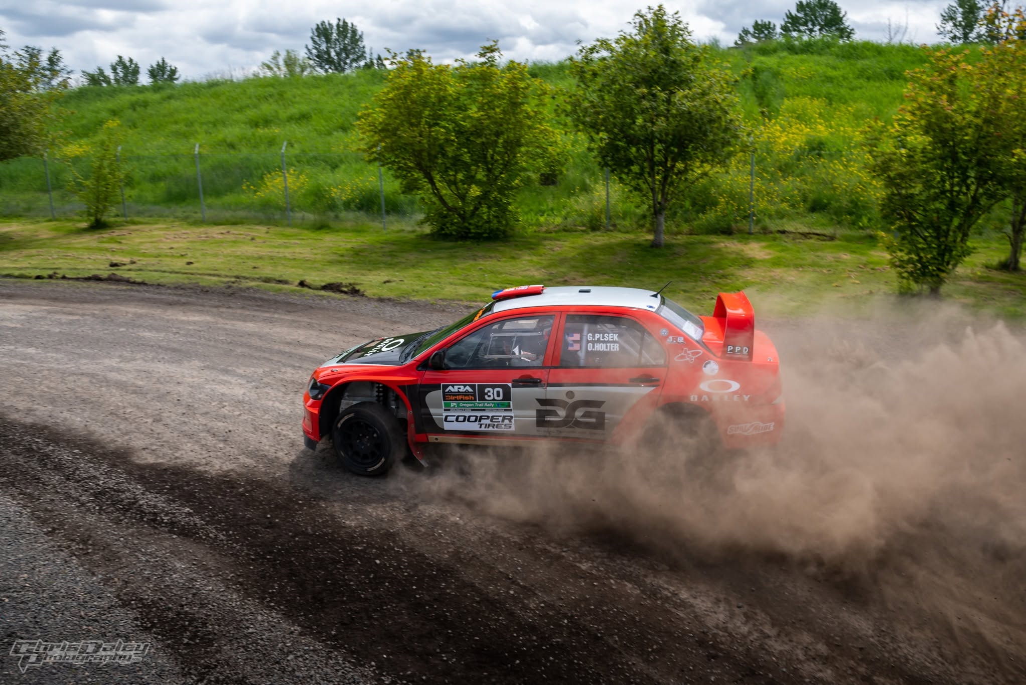 The red Mitsubishi sliding through a gravel hairpin with a wall of dust behind it