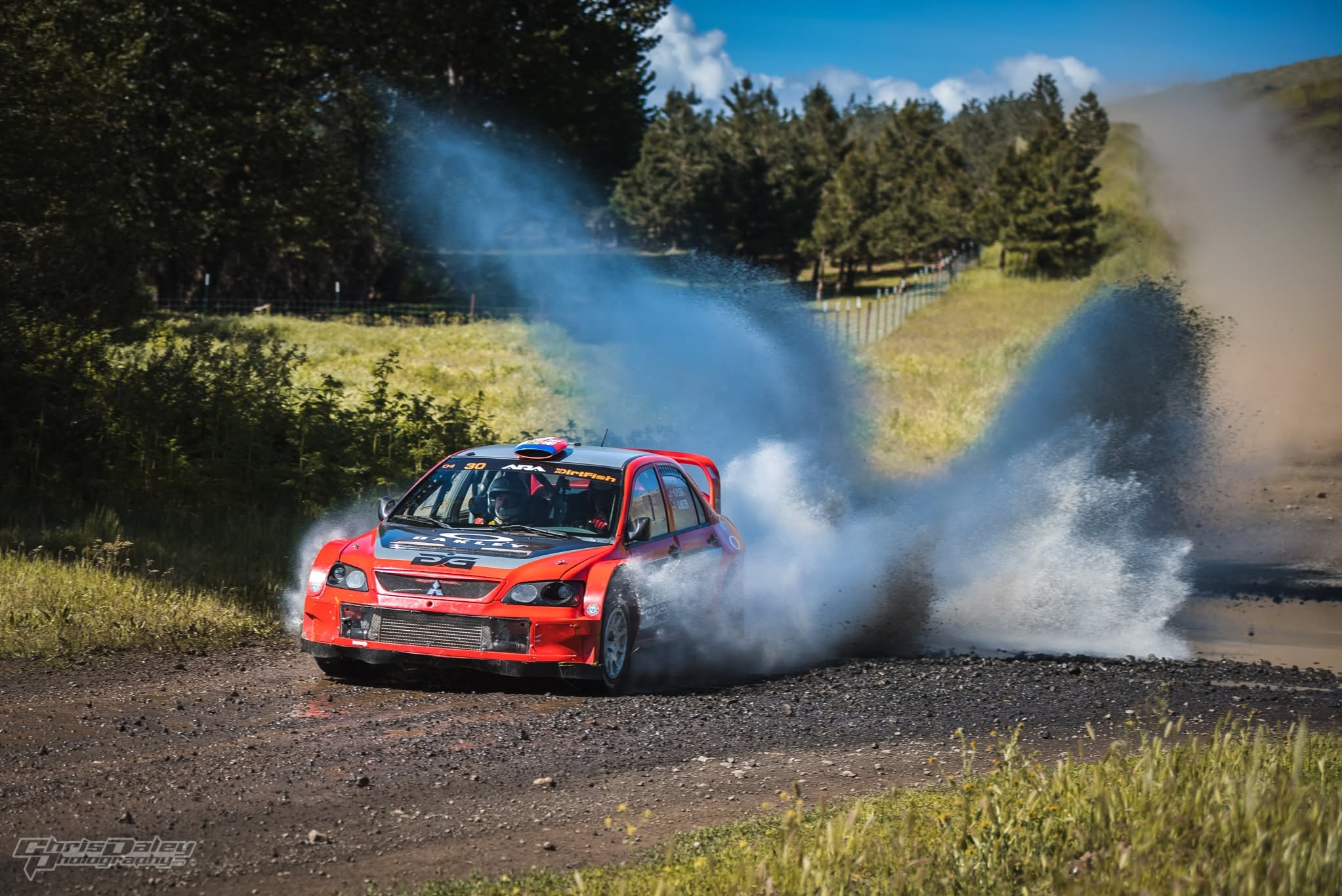 The red Mitsubishi blasting through a water splash, spray fanning out behind it