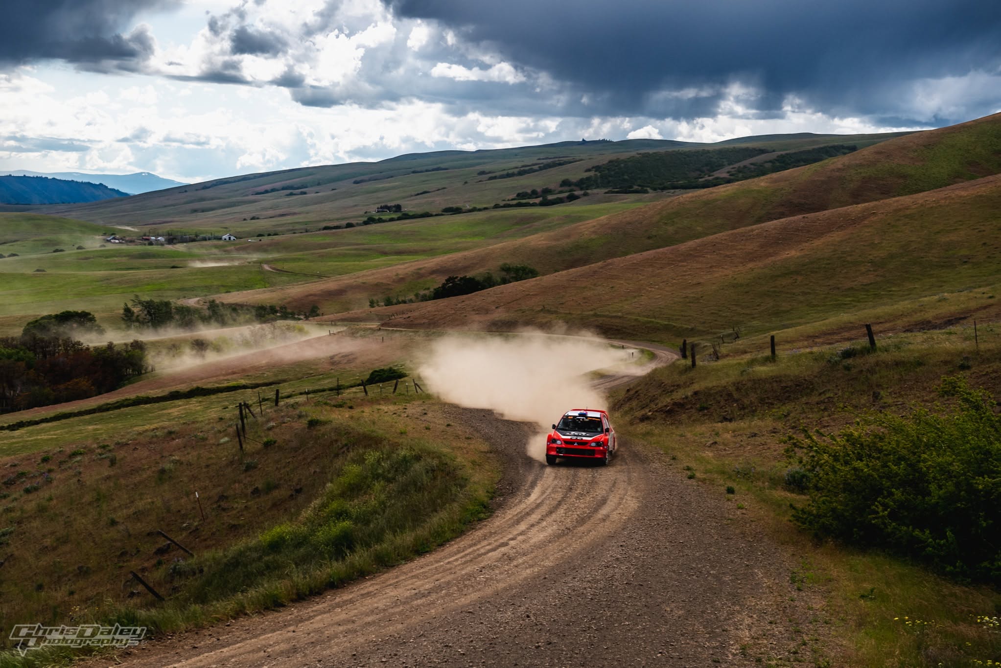 The red TMS Mitsubishi throwing up a dust trail on a gravel stage through open rolling hills