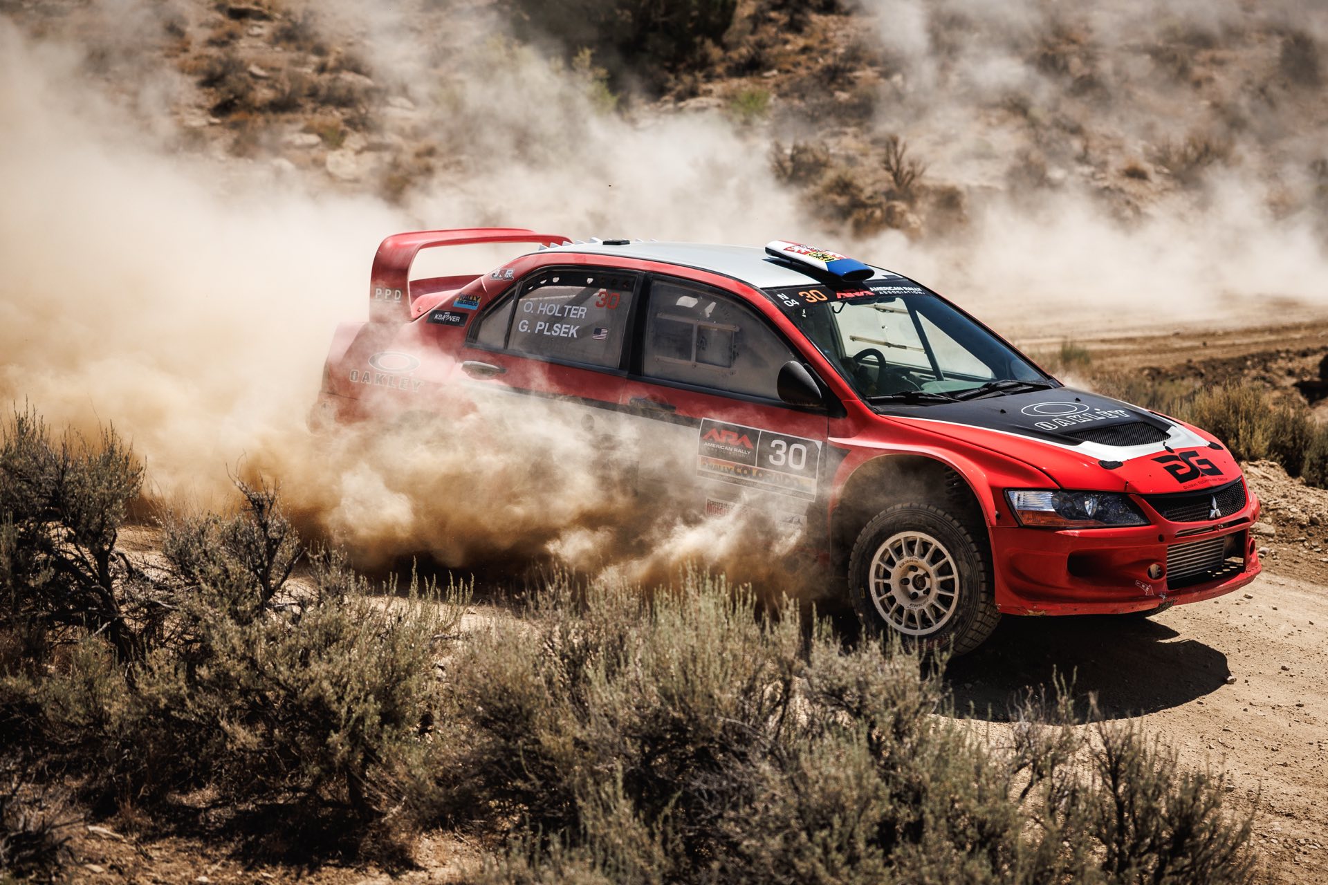The red number 30 Mitsubishi sliding through a gravel corner in a cloud of dust at Rally Colorado 2025