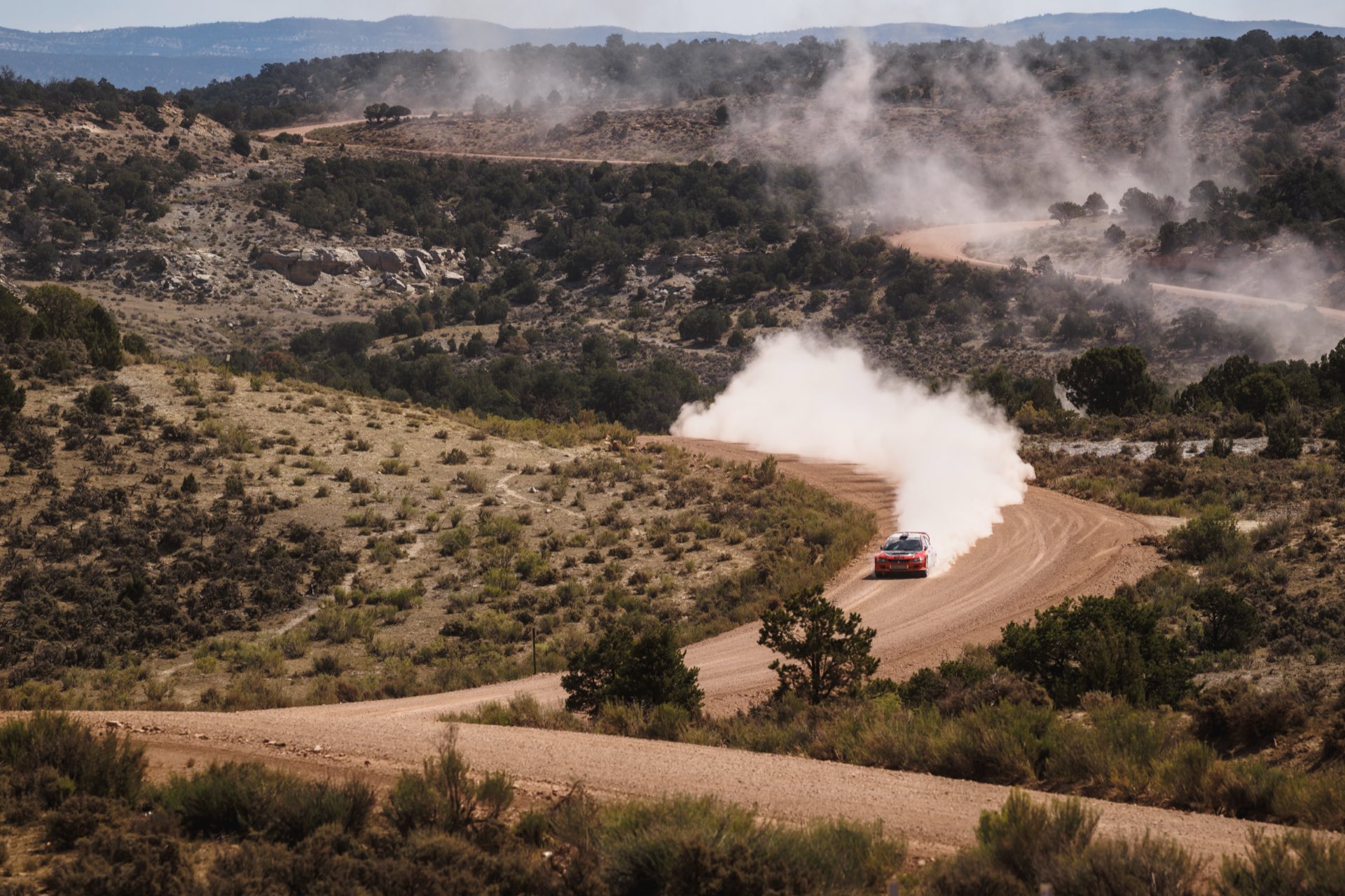 The red TMS Mitsubishi trailing a plume of dust on a winding gravel stage through high desert hills at Rally Colorado 2025