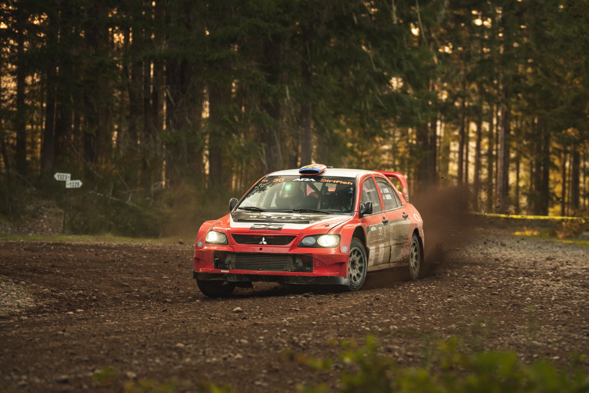 The red number 30 Mitsubishi cornering with headlights on through a dark forest stage at the 2022 Olympus Rally